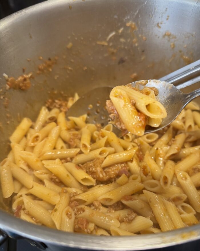 Barilla gluten-free penne tossed with Papa Sandemano’s Family Sauce in a stainless-steel pot.